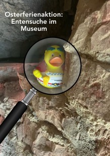 Eine Badeente ist in einer Mauer versteckt, darüber eine Lupe.