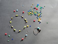 Auf einem dunklen Tisch liegen viele bunte Perlen unterschiedlicher Formen und Größen. Einige sind zu einem Armband gebunden.