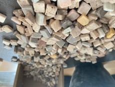 Unzählige kleine Steinchen in Erdtönen fallen aus einer Holzschachtel heraus und liegen auf dem Tisch.
